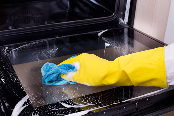 Close-up of hands scrubbing oven door glass with eco-friendly soap and sponge.